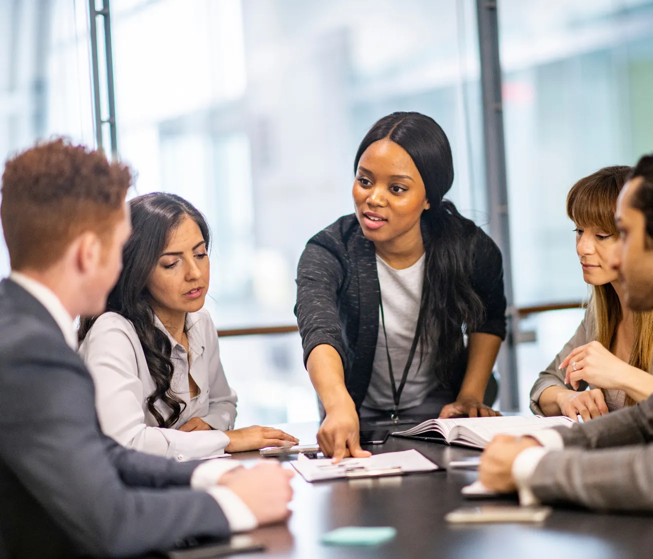 A woman leads a business meeting, pointing at a document as colleagues listen attentively around a table.