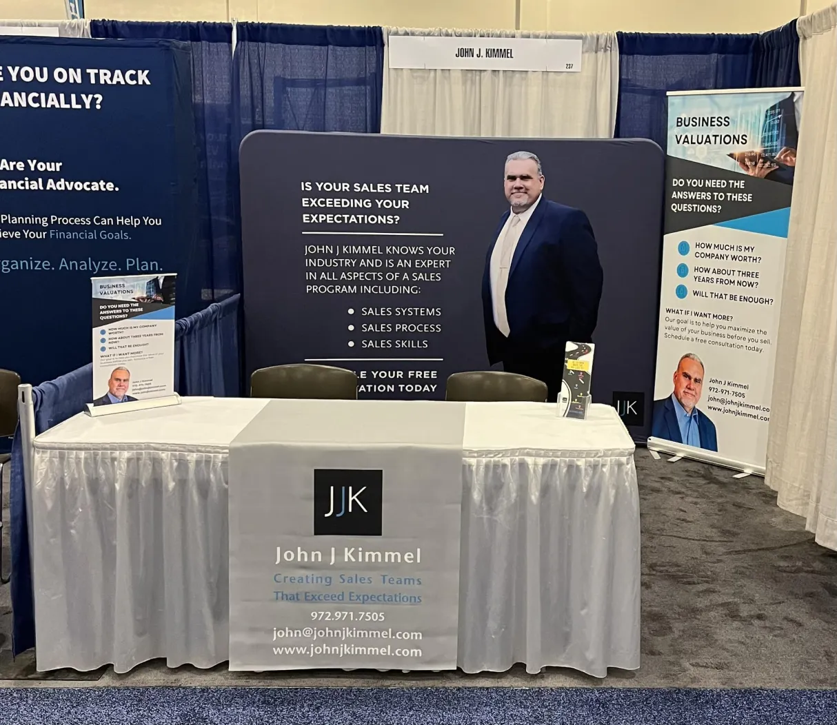 why-1 Trade show booth for John J. Kimmel, featuring banners, business cards, and a large photo of John J. Kimmel.